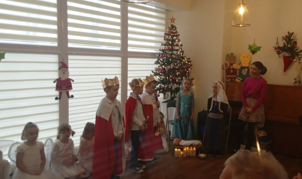 Trzej królowie witają się z Maryją i Józefem. W tle udekorowana choinka.