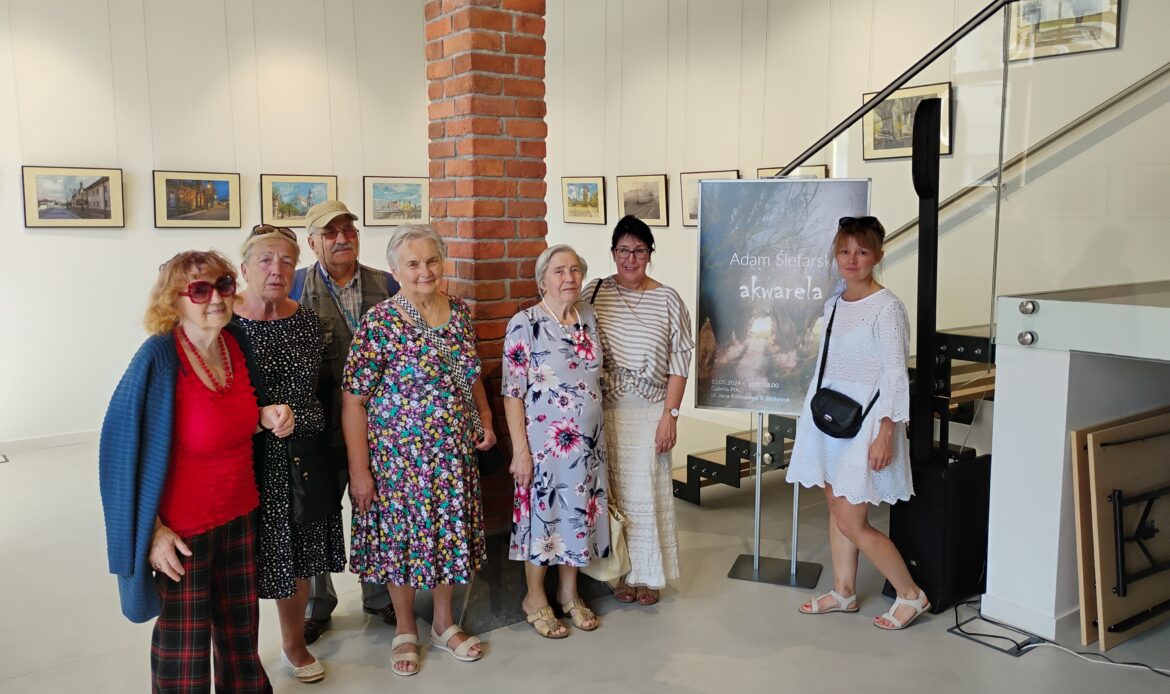 Grupa seniorów razem z opiekunkami na wystawie akwareli.
