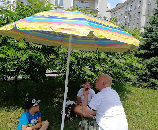 wychowawca i dzieci pod parasolem w ogrodzie świetlicy
