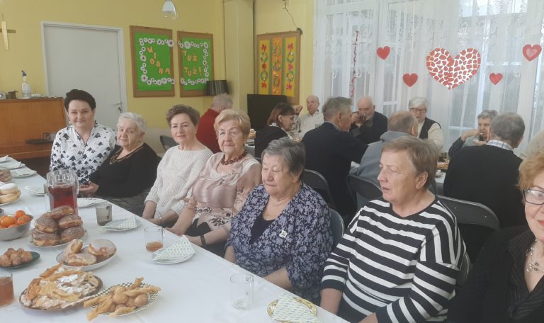 Seniorzy siedzą przy stole z pączkami i faworkami
