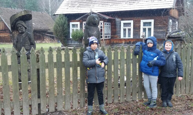 Chłopcy na tle figur rzeźbionych w drewnie i wiejskiej chaty