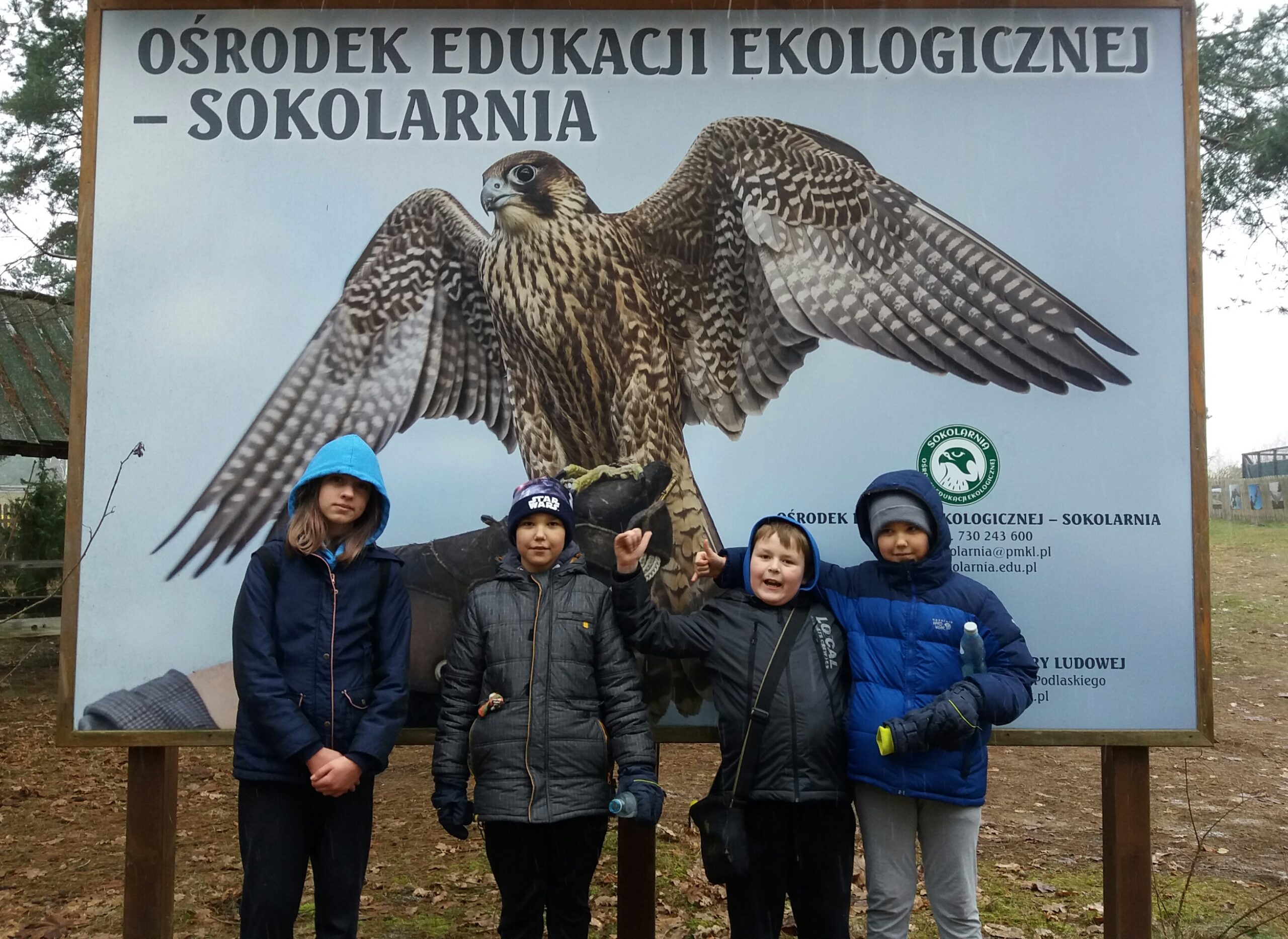 Czworo dzieci na tle baneru Ośrodka Edukacji Ekologicznej - Sokolarnia