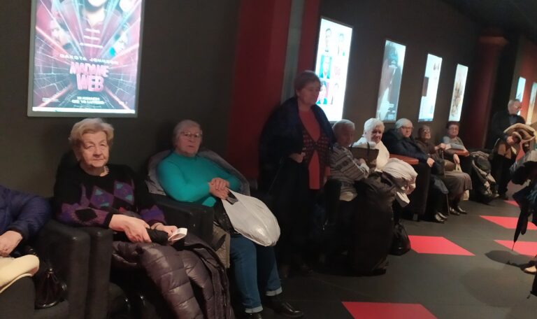 Grupa seniorów na korytarzu kina oczekująca na seans filmowy.