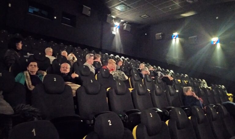 Grupa seniorów na sali kinowej przygotowują się do projekcji filmu.