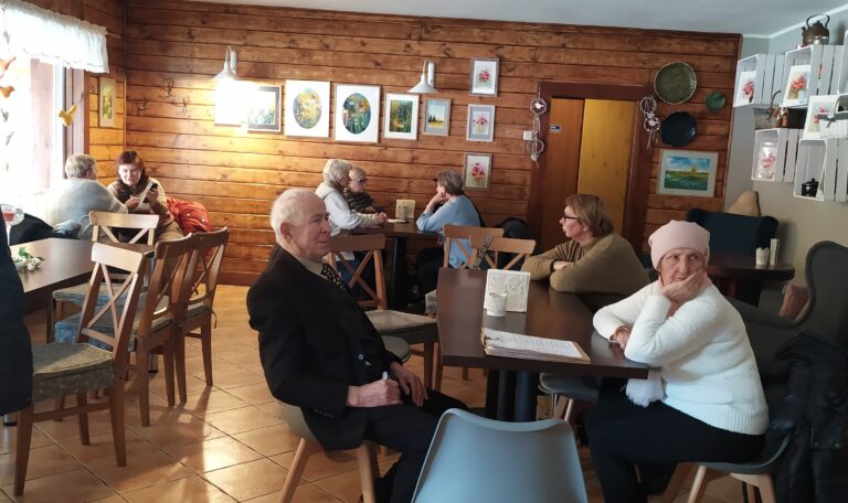 Seniorzy siedzą przy stolikach w oczekiwaniu na pyzy w restauracji Supraśl.