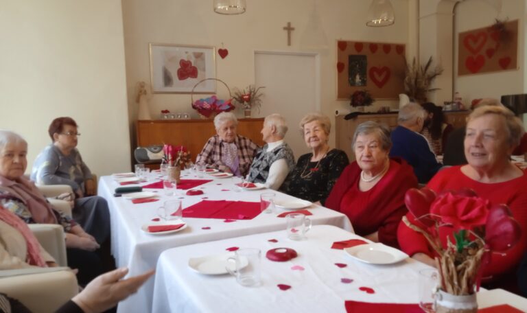 Grupa osób siedzi przy udekorowanym stole, dominuje kolor czerwony.