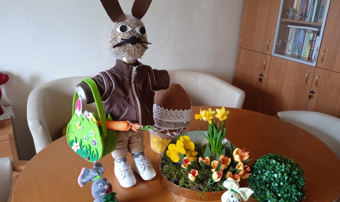 Wielkanocna dekoracja składająca się z dużego królika w dziecięcych ubrankach, krokusów i zajączków ze skarpetek.